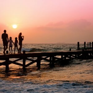 Silhouetted family enjoys a stroll on the beach pier at a vibrant sunset over the ocean waves.