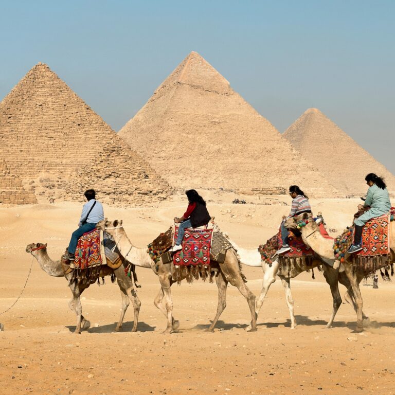 Tourists riding camels near the Great Pyramids of Giza, Egypt under clear skies.