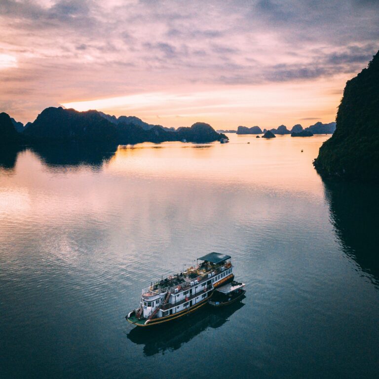 Drone shot of a cruise ship navigating the serene waters of Halong Bay, Vietnam, at sunrise.